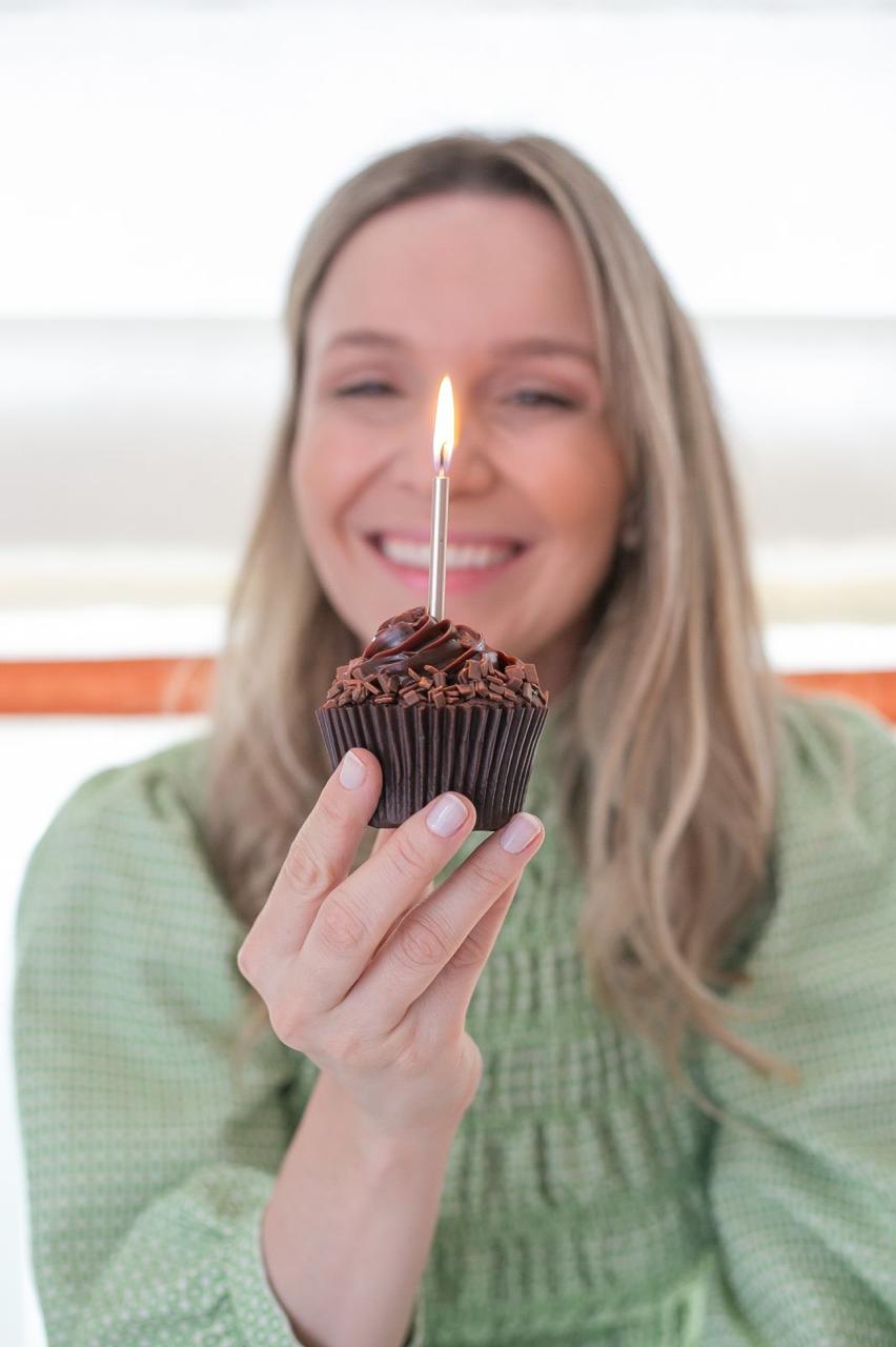 Helen Marini sorrindo com um cupcake aceso em uma celebração da Aurora Bebê.