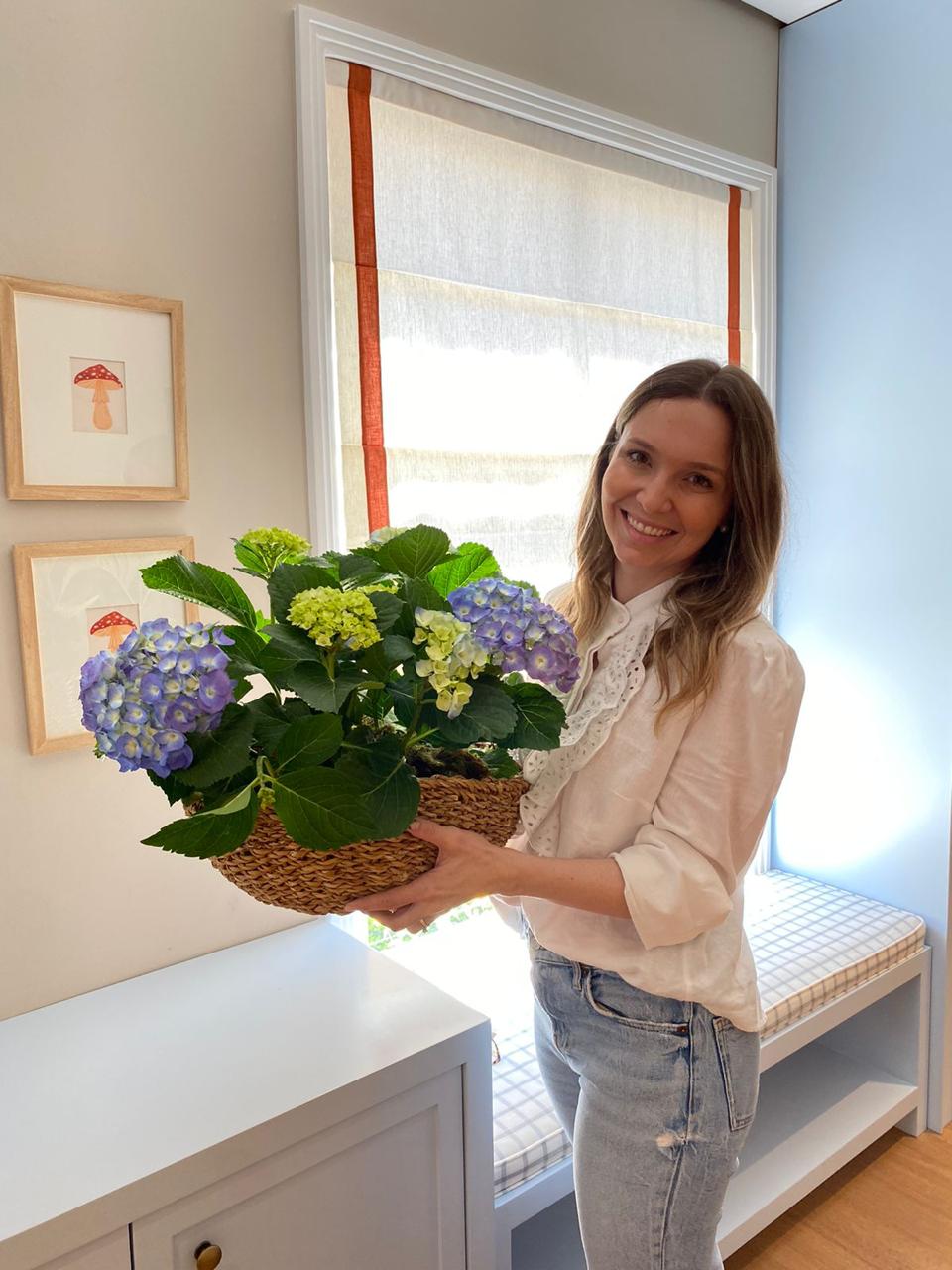 Helen Marini segurando flores em um ambiente delicado da Aurora Bebê.